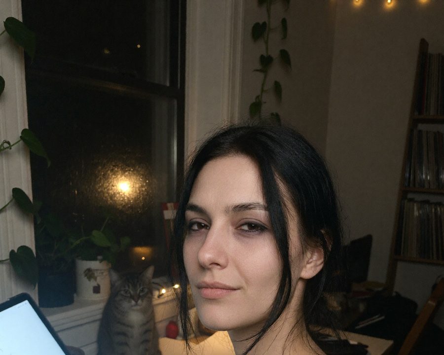 Nova at her drawing desk late at night, her cat on the windowsill behind her.